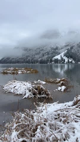 Tranquil winter landscape featuring a snowy lake surrounded by mountains and forests