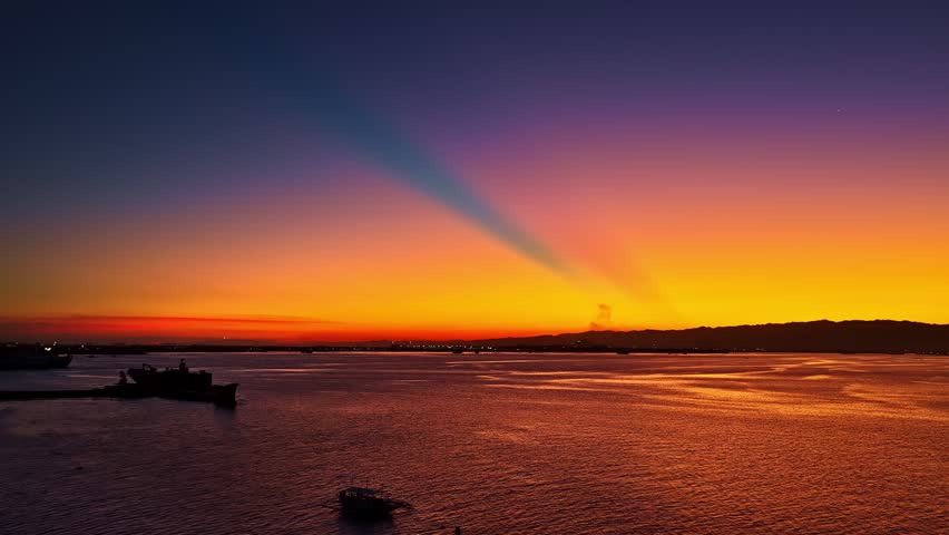 Aerial view of a vibrant sunset over calm sea near Dusit Thani Mactan Cebu resort, with boats on the water and colorful clouds reflecting on the horizon.
