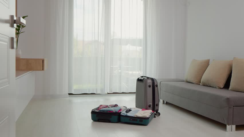 A woman wears headphones and dances next to a suitcase filled with clothes in a bright room. She enjoys the moment as she prepares for her upcoming trip.