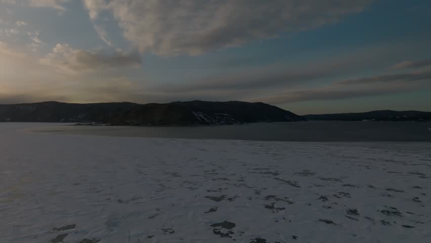 Aerial footage of a frozen shoreline and glowing sunset at the Angara River outflow into Lake Baikal near Listvyanka, Irkutsk Oblast, Russia