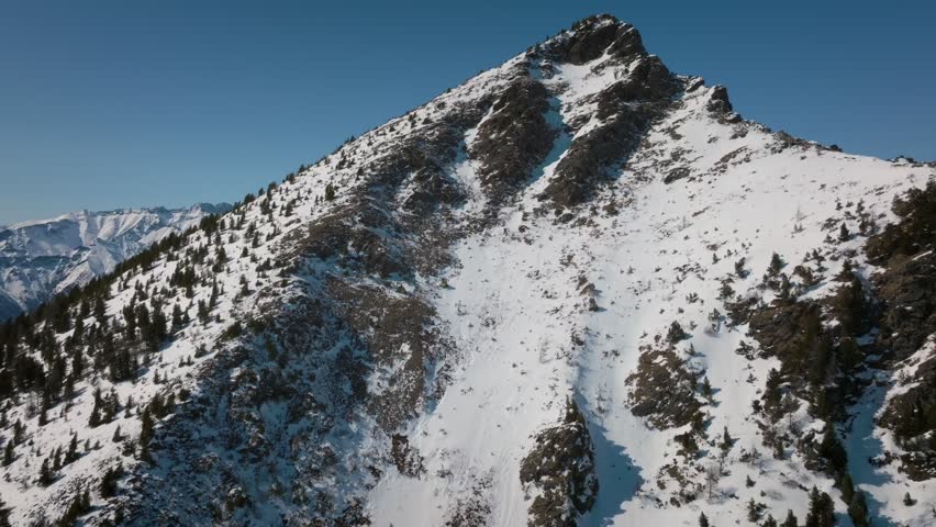 Aerial footage of rugged snow-covered mountain ridge and peaks under clear blue sky near Arshan village, Republic of Buryatia, Russia, winter wilderness landscape