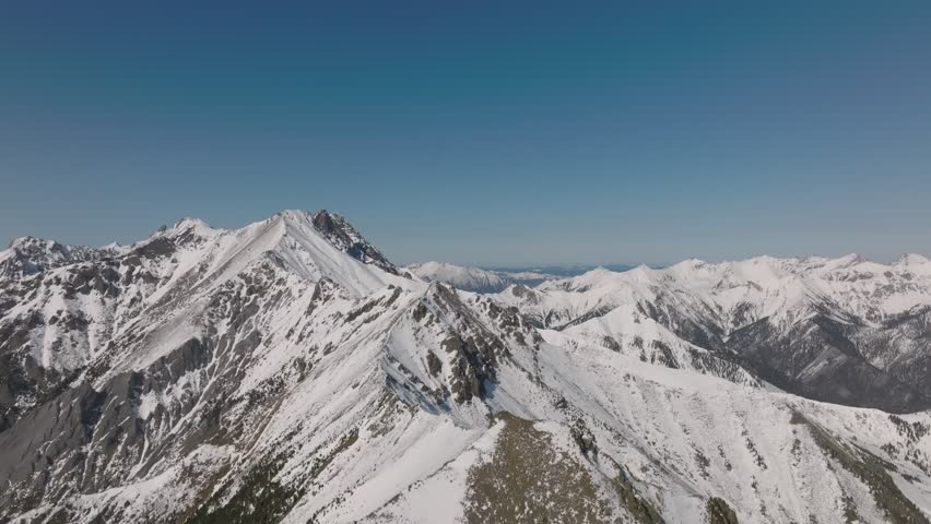 Drone footage of rugged snow-covered mountain ridge and peaks under clear blue sky near Arshan village, Buryatia, Russia, scenic winter landscape in Siberia