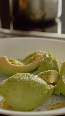 Vertical Screen: Seasoning fresh avocado pieces with salt, pepper, and oil to prepare a flavorful guacamole. Perfect for enhancing dishes or enjoying with chips.