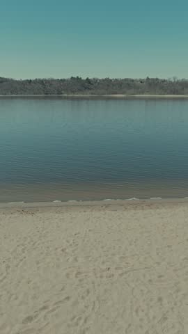 Low aerial sideways flight along empty sandy St Croix River beach in Hudson Wisconsin reveals gentle ripples, footprints in sand and forested Minnesota shoreline opposite