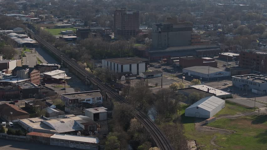 Aerial view of industrial buildings and a long railway track surrounded by trees and urban infrastructure in Louisville, Kentucky, United States.