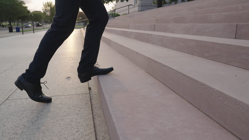 Business man walking up stairs with ambition. Businessman climbing steps for business growth. Business man advancing stairs in outdoor city. Businessman walking stairs toward career goal.