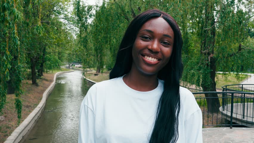 Smiling woman stands by a park river in daylight enjoying nature and the outdoors with trees around
