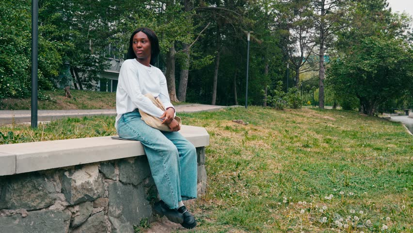 Person sitting on a stone wall in a park with trees and grass around during the daytime