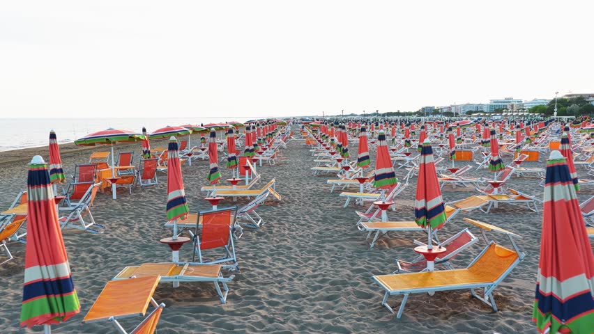 Deserted sandy beach with rows of closed umbrellas and empty sunbeds during an early morning