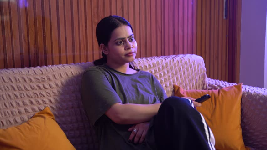 Indian Woman Watching TV and Relaxing on Sofa with Remote Control at Home