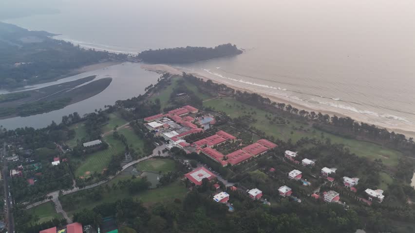 Wide cinematic aerial of Golf Ground and Spa Resort Goa showcasing structured resort blocks, coastal greenery, calm backwaters, and an uninterrupted shoreline stretching into the horizon.