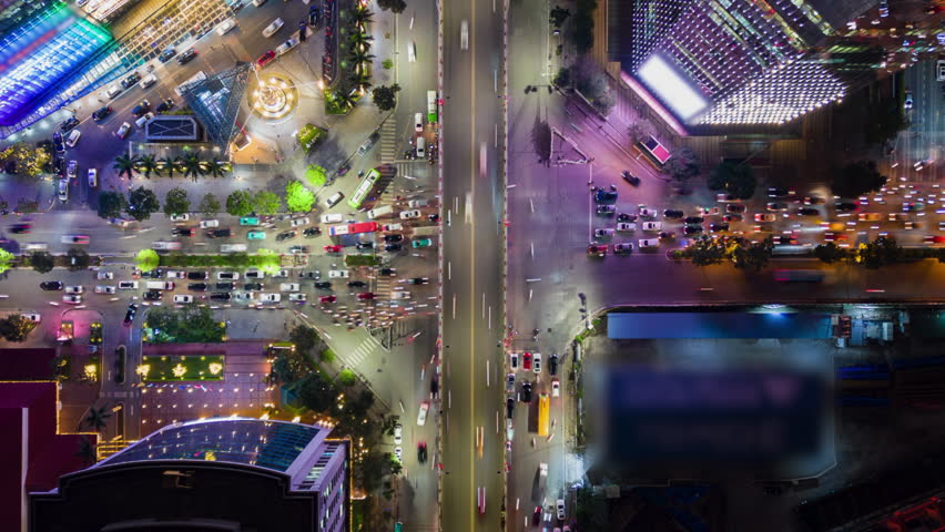 Aerial top down night timelapse of busy city traffic in Hanoi, Vietnam with illuminated intersections, moving cars, colorful lights, and vibrant urban life in Southeast Asia.