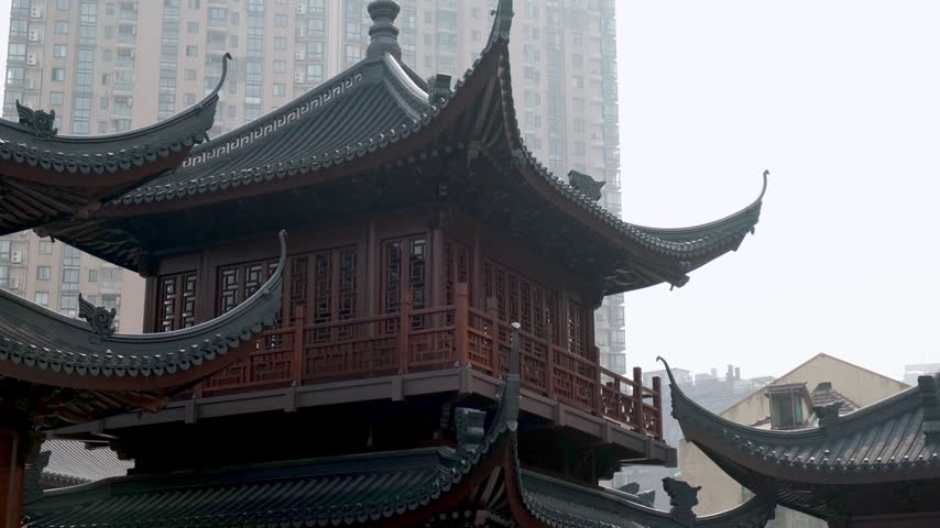 A traditional Chinese pavilion stands in stark contrast against a modern high-rise apartment building on a misty day.