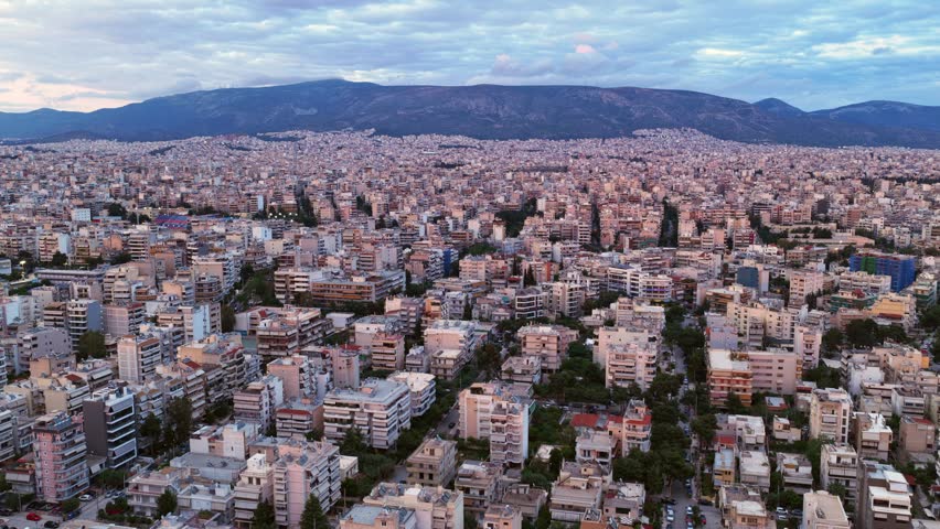 Sweeping aerial view of athens, greece, showing the dense urban sprawl of residential buildings with the iconic mount hymettus rising in the background under a cloudy evening sky