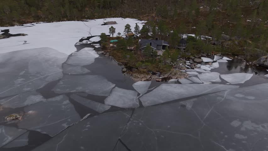 Cabin sits on small island in lake with ice cracking as sun sets in late afternoon.