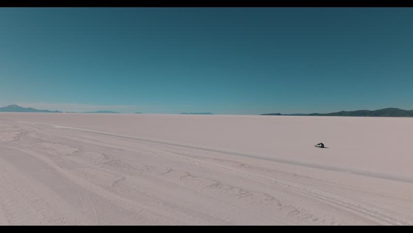 4x4 vehicle driving across the Uyuni salt desert in Bolivia, crossing vast white plains under a clear sky. Minimalist landscape with endless horizon and remote travel adventure.
