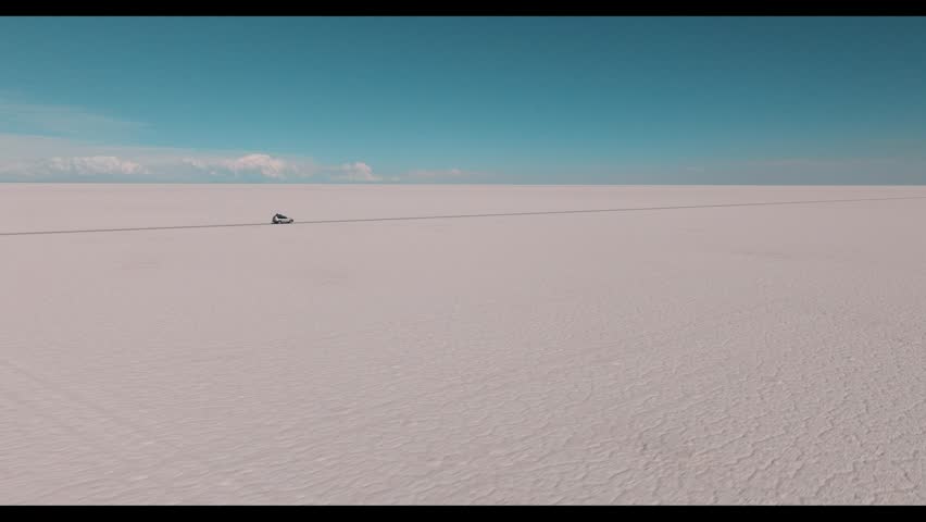 4x4 vehicle driving across the Uyuni salt desert in Bolivia, crossing vast white plains under a clear sky. Minimalist landscape with endless horizon and remote travel adventure.