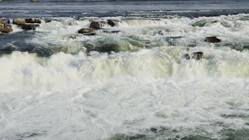 Fast flowing river rapids crashing over dark rocks with foamy white water, strong natural current movement and dramatic outdoor landscape scenery!