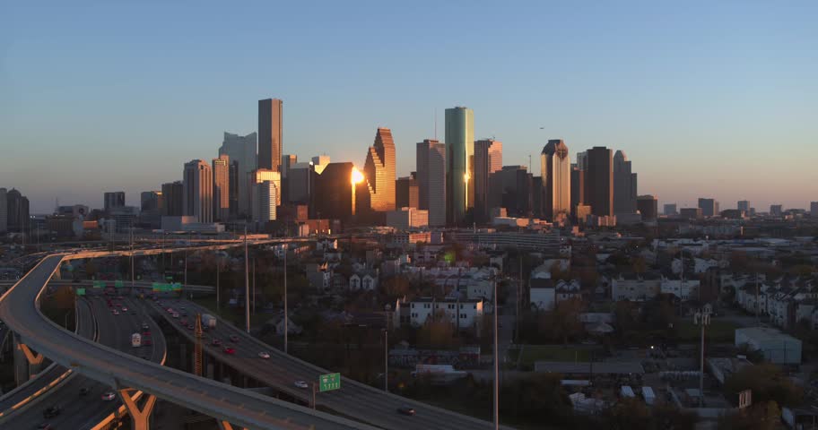 Dynamic aerial footage captures Houston skyline during golden hour sunrise. Busy highway traffic and urban sprawl under clear sky. Cinematic motion.