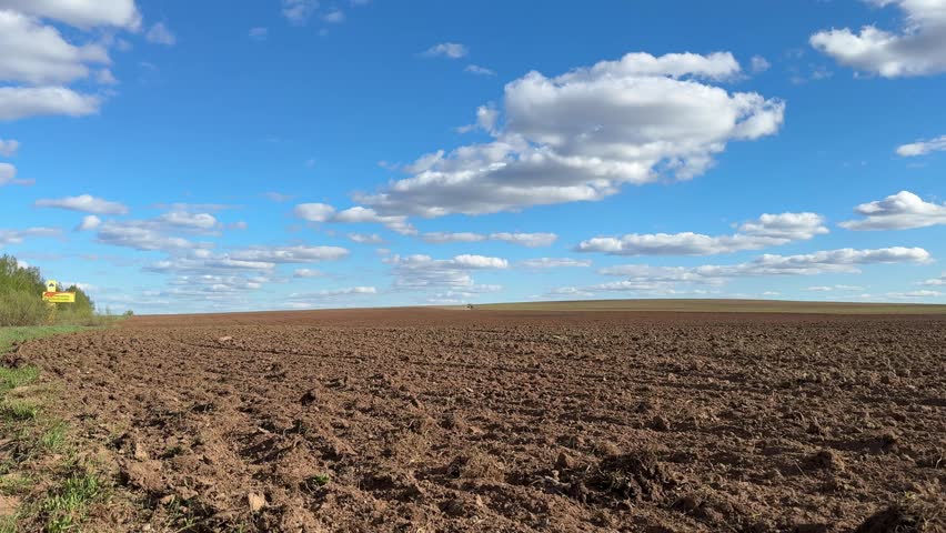 Open field under a clear blue sky with scattered clouds