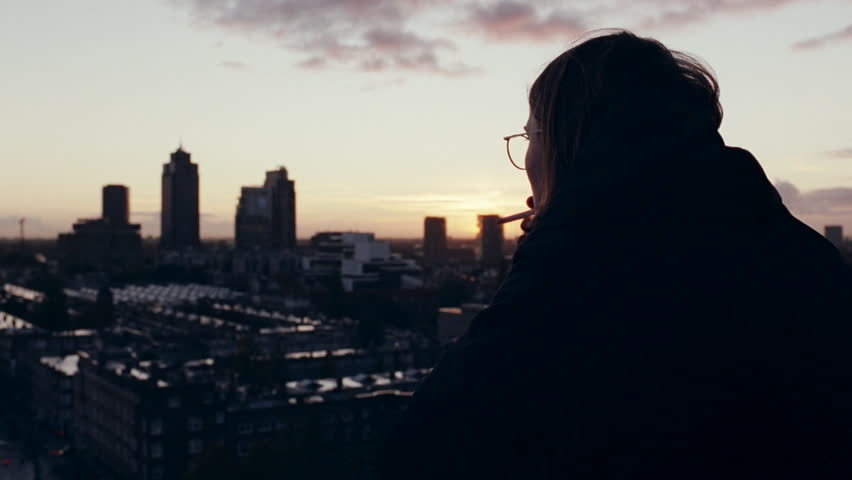 Thoughtful woman with glasses in silhouette looking at the Amsterdam skyline during a beautiful sunset