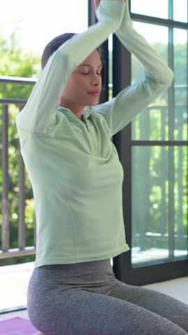 Vertical video: Pressing palms she mint top on balcony mat moving hands heart-belly calming breath. Meditation, mindfulness, serenity, yoga, sunlit, outdoors, vertical video