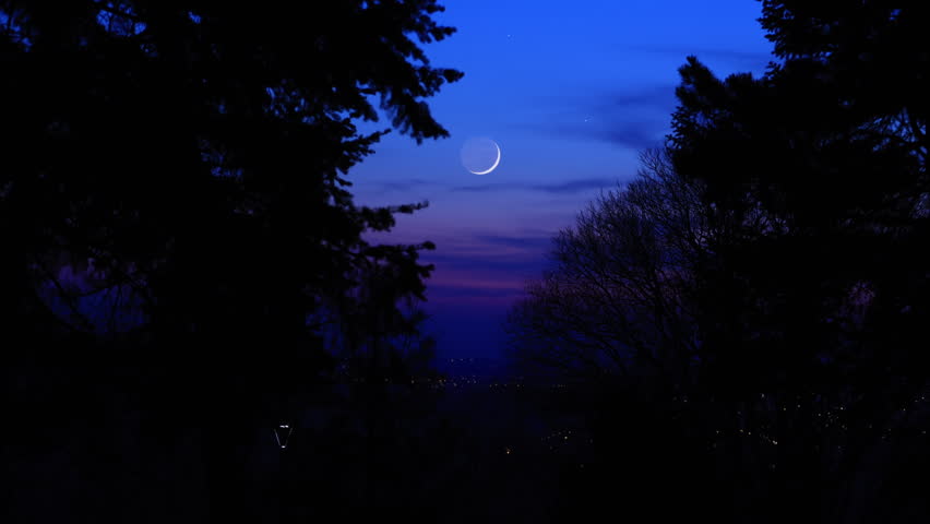 Blue hour time with crescent Moon, stars and planets above landscape silhouettes.
