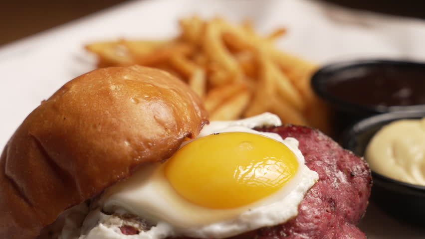 Appetizing burger with bacon, a fried egg, and french fries served on a platter, fa01