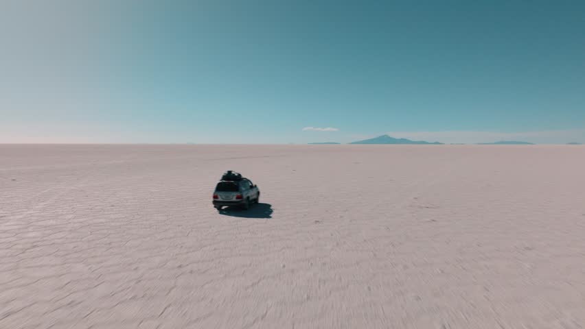 4x4 vehicle driving across the Uyuni salt desert in Bolivia, crossing vast white plains under a clear sky. Minimalist landscape with endless horizon and remote travel adventure.