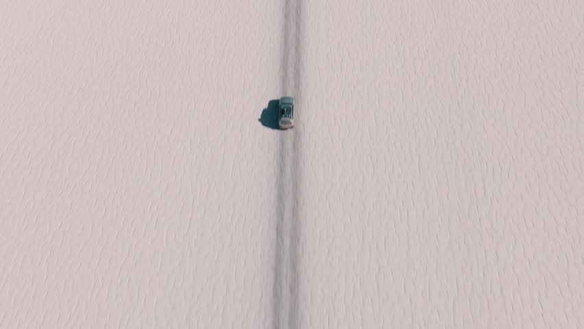 4x4 vehicle driving across the Uyuni salt desert in Bolivia, crossing vast white plains under a clear sky. Minimalist landscape with endless horizon and remote travel adventure.