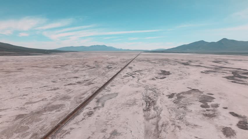 Aerial view of railroad tracks crossing Salar de Chiguana in Bolivia, cutting through vast salt desert. Minimalist landscape with endless horizon in the remote Altiplano.