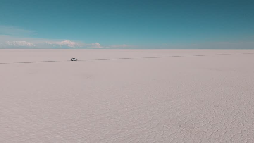 4x4 vehicle driving across the Uyuni salt desert in Bolivia, crossing vast white plains under a clear sky. Minimalist landscape with endless horizon and remote travel adventure.