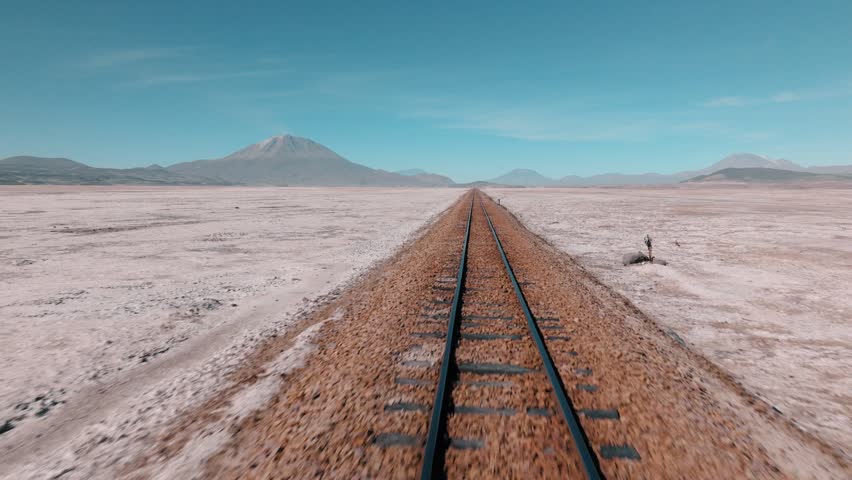 Aerial view of railroad tracks crossing Salar de Chiguana in Bolivia, cutting through vast salt desert. Minimalist landscape with endless horizon in the remote Altiplano.