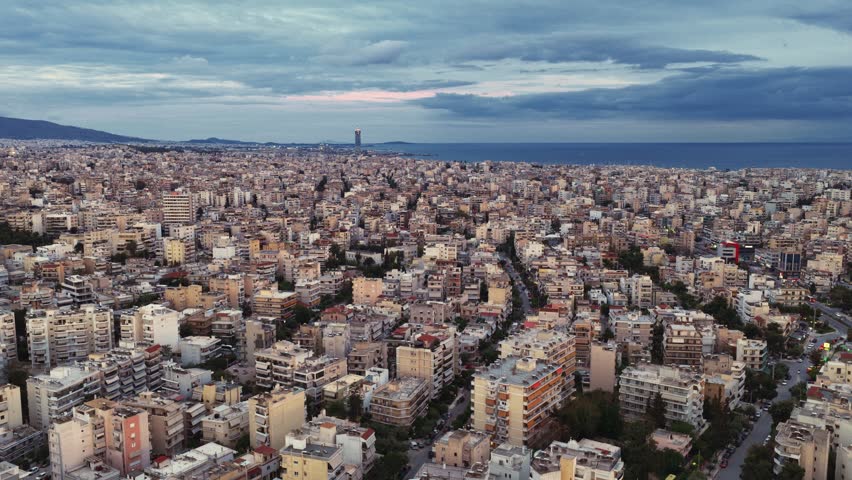 Expansive aerial view showing the dense urban cityscape of thessaloniki, greece, with countless buildings stretching towards the sea under a dramatic cloudy sky during the evening hours