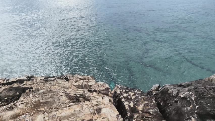 A rocky shoreline along calm clear water on a sunny day.