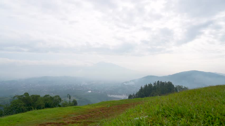 Beautiful landscape of green hills and misty mountains under a cloudy sky.