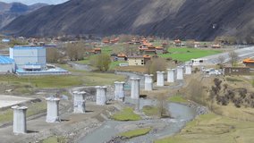 Ongoing construction of concrete bridge piers for the Sichuan-Tibet Railway in a scenic mountain valley with rural settlements and green fields. - Powered by Shutterstock - Get 15% off with code: PIKWIZARD15