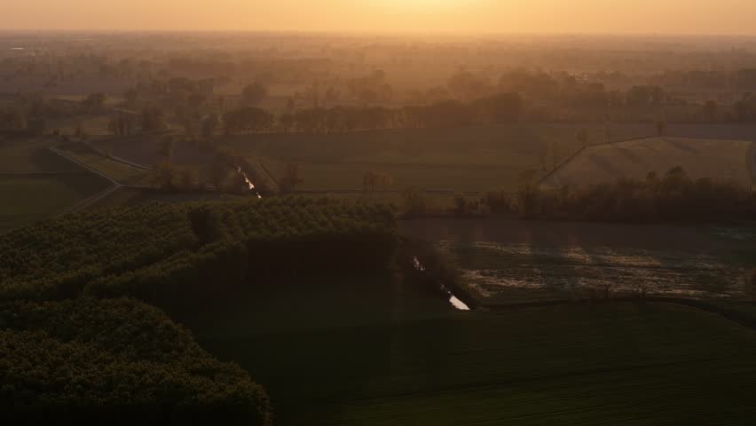 Expansive springtime landscape of the Po Valley with agricultural fields, trees, and water channels bathed in warm sunset light