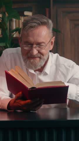 Inspired Caucasian old senior business man enjoying reading interesting book taking off glasses looking at camera joy laughing smile citizen smiling retired businessman male read literature at office