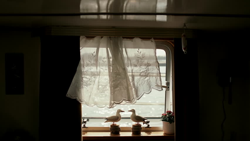 White curtain flowing in the breeze inside a houseboat cabin with a view of shimmering water
