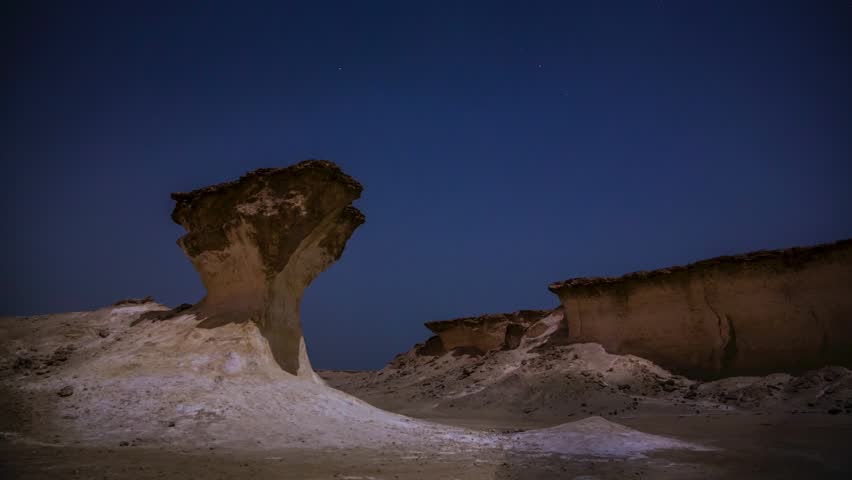 Night timelapse of moonlit rock formations in Zekret Qatar with rotating stars and shifting lunar shadows across desert landscape