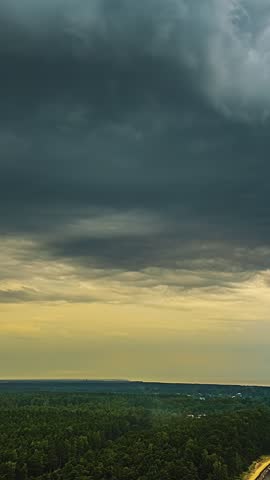 Dramatic storm clouds rapidly move over a dense green forest in late afternoon light