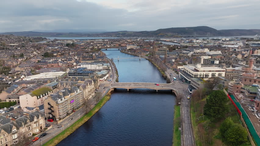 Aerial footage over Inverness city, Scotland, cloudy day, flying over River Ness, historic bridges, Highland capital skyline, grey overcast sky above