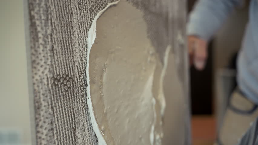 Professional worker applies thick layer of adhesive to ceramic tile to glue it to wall. renovation, building preparation, and construction tools 