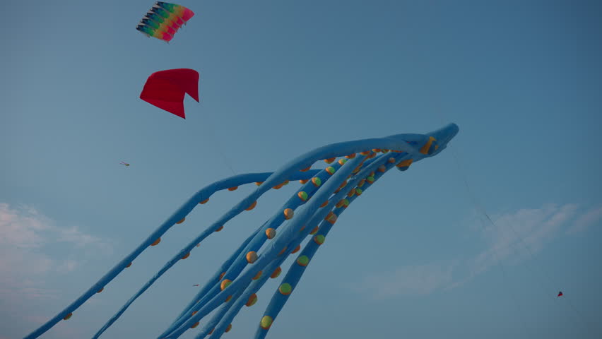 Colorful kite festival with giant inflatable kites flying in blue sky, outdoor event with large animal shaped squids and whales floating in wind under clouds 4k