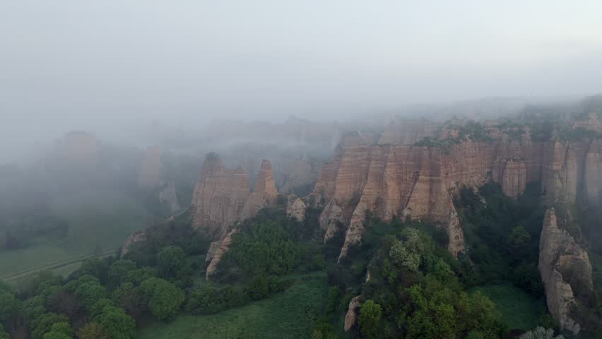 Aerial view of the Valdarno rock formations shrouded in thick fog and mist above green forests in Florence, Tuscany, Italy.