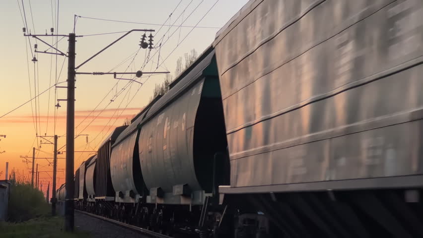 Freight Train Moving at Sunset with Tank and Cargo Wagons | Railway Infrastructure with Electric Poles and Wires | Industrial Logistics and Transportation Close-Up Side View