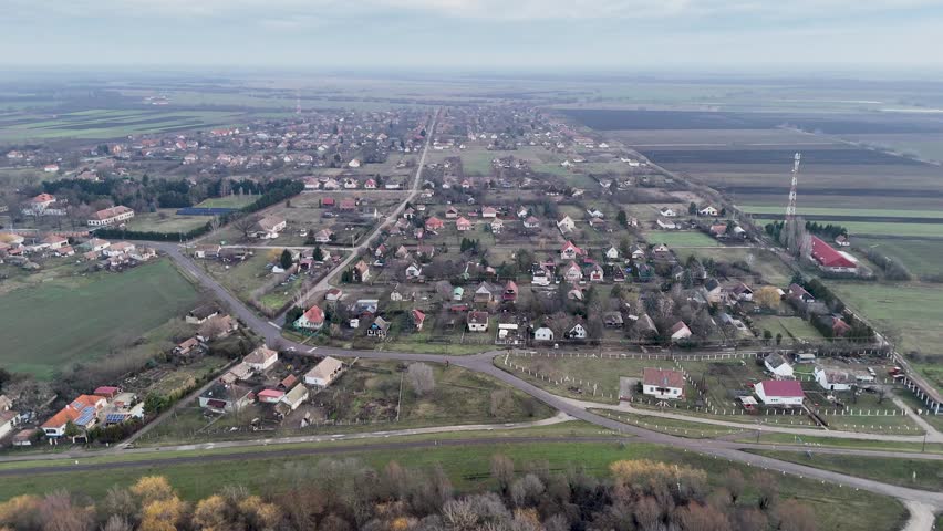 Aerial view of the rural village of Tiszasuly featuring residential houses, gardens, and surrounding agricultural fields under a cloudy sky in Tiszasuly, Hungary.