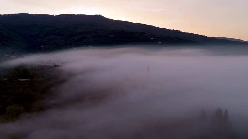 Aerial view of the Valdarno valley shrouded in thick morning mist with a church steeple emerging from the fog at dawn in Florence, Tuscany, Italy.