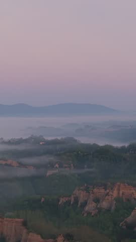 Aerial view of the Balze del Valdarno rock formations with thick fog rolling over the hills and forests at dawn in Florence, Tuscany, Italy.